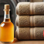 A bottle of apple cider vinegar next to an apple and folded, clean towels. A washing machine in the background.
