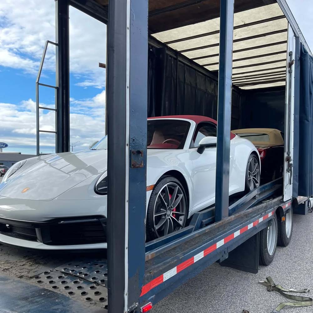 White Porsche sports car secured inside an enclosed auto transport trailer with protective strapping, showing premium enclosed shipping service