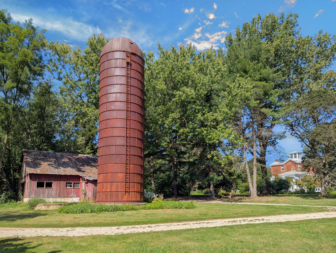 A weathered red barn and tall cylindrical silo on Brampton 1860's property, with the historic Manor House visible in the background, showcasing the estate's agricultural heritage.