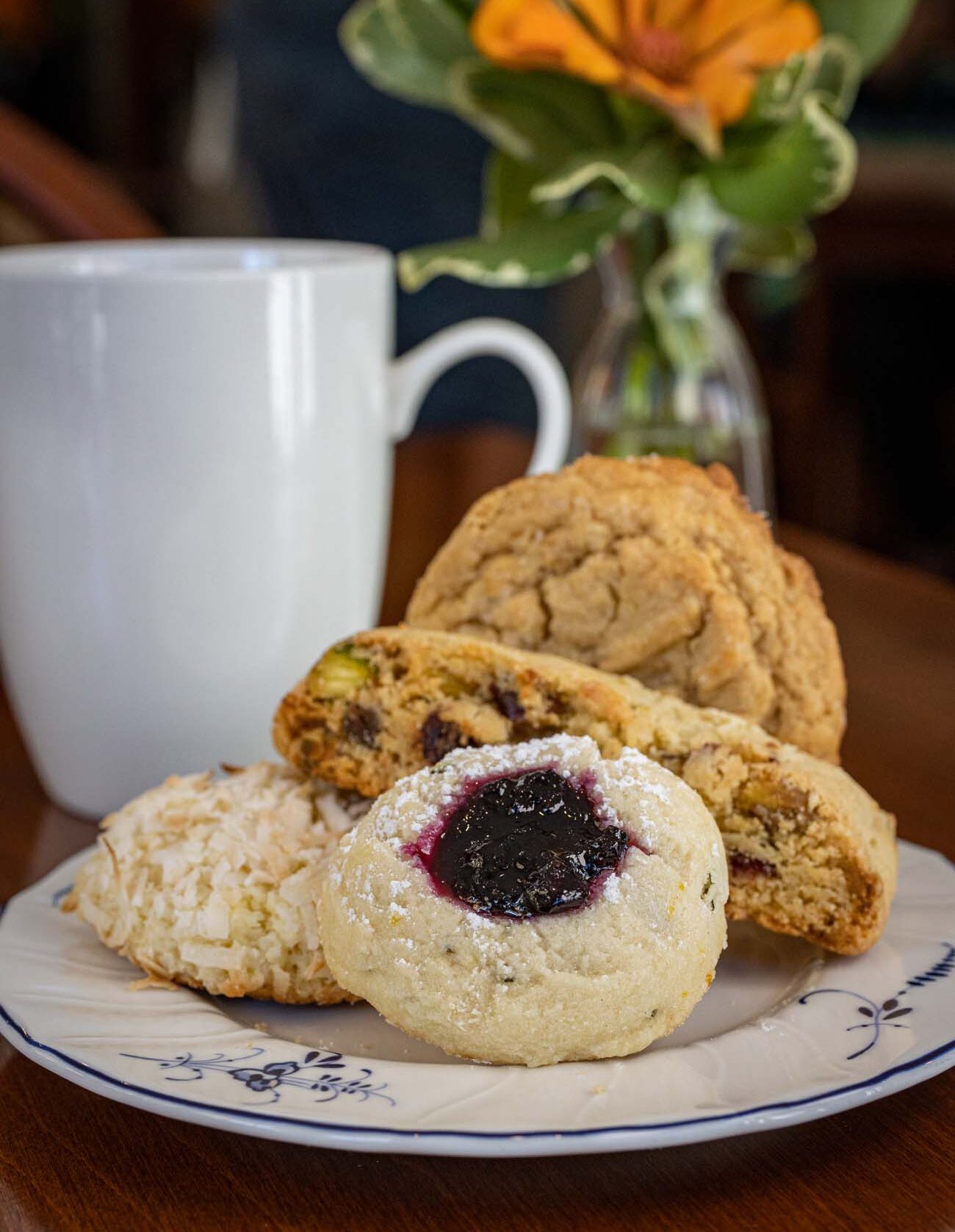 An assortment of fresh-baked tea time pastries including scones, muffins, and Danish on a Brampton-branded plate, with coffee cup and small flower arrangement.