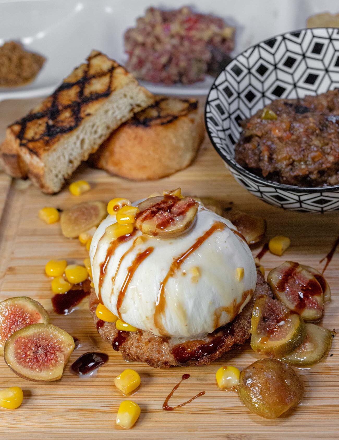 An elegant appetizer plate at The Kitchen at the Imperial featuring burrata cheese over fried green tomatoes with grilled figs, balsamic reduction, and microgreens.