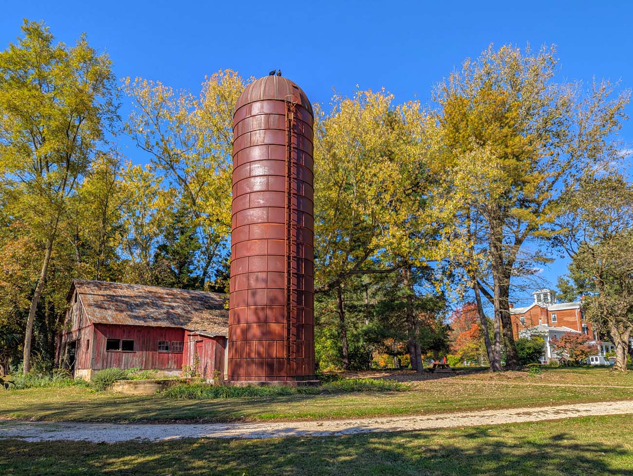 Rustic red barn and tall brick silo on Brampton property with fall trees in background, showing the estate's agricultural heritage