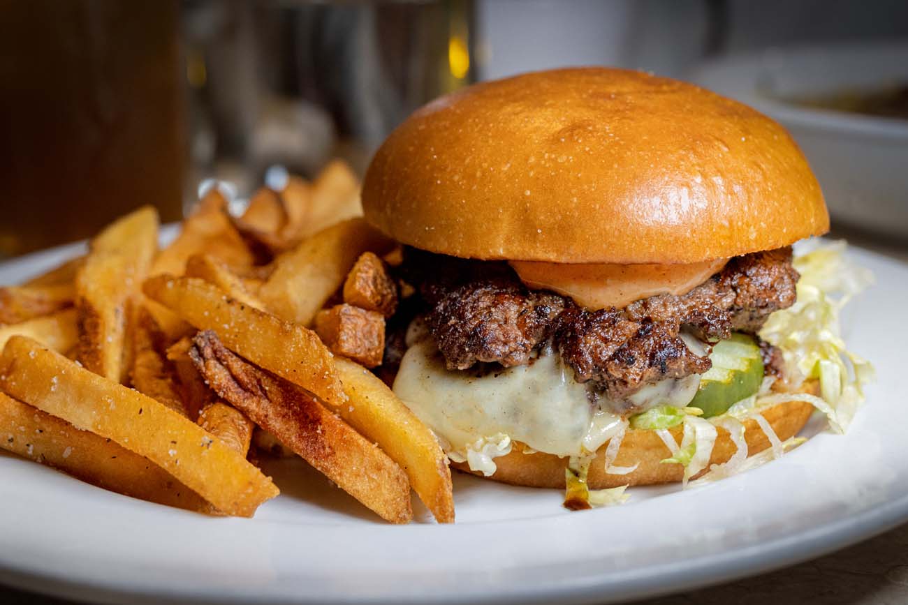 hick burger with melted cheese on brioche bun with lettuce and special sauce, served with generous portion of golden french fries on white plate, restaurant setting