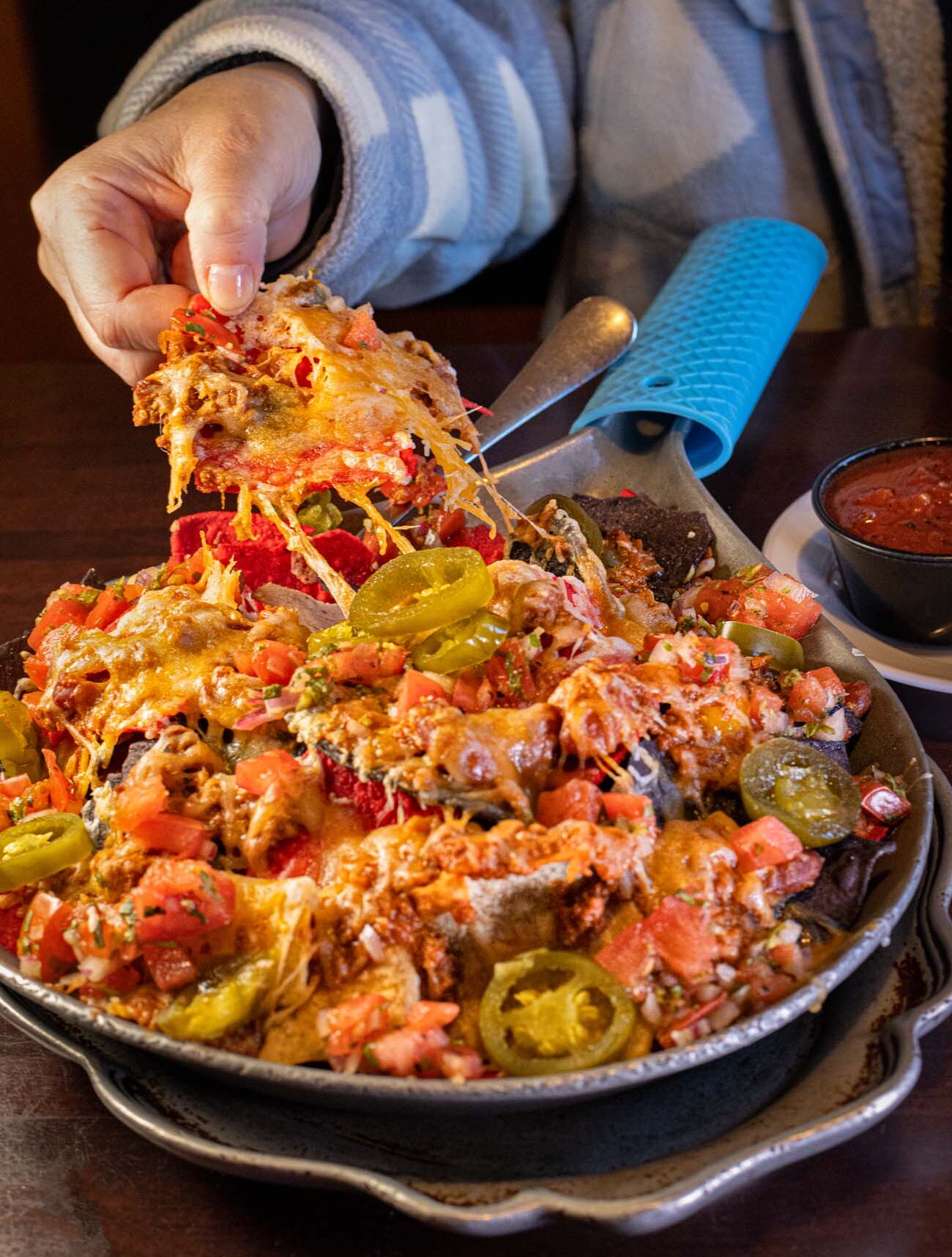 Loaded appetizer nachos with melted cheddar cheese, jalapeños, tomatoes, black olives and sour cream being lifted with cheese pull at Apple Valley Restaurant in Milford, Pennsylvania Pocono Mountains