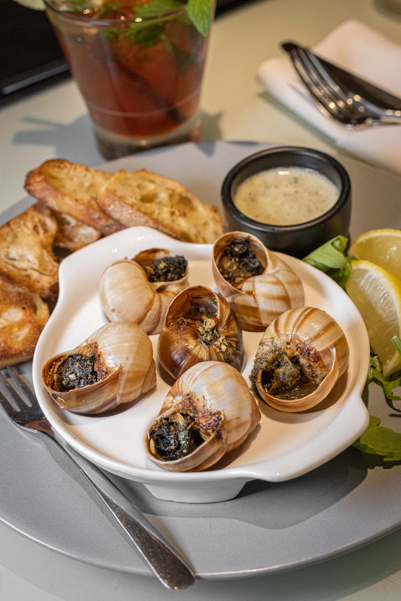 Classic French escargot appetizer in Burgundy snail shells with garlic herb butter, grilled baguette toasts, and craft cocktail at Bar Louis underground brasserie in Hotel Fauchere Milford Pennsylvania