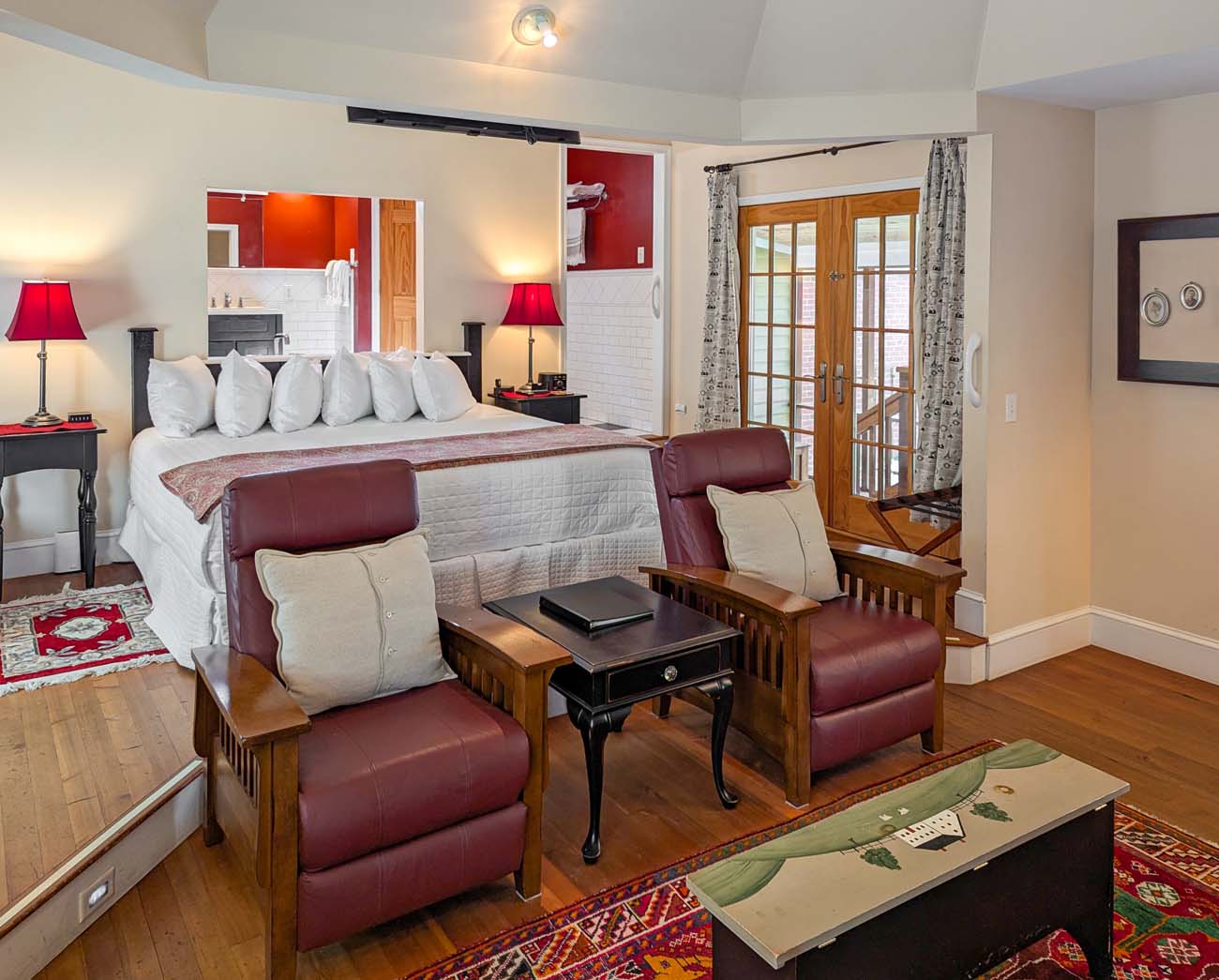 Inside Marleys Cottage at Brampton 1860 with king bed, cozy furnishings, red accent wall, fireplace, and French doors opening to a private patio