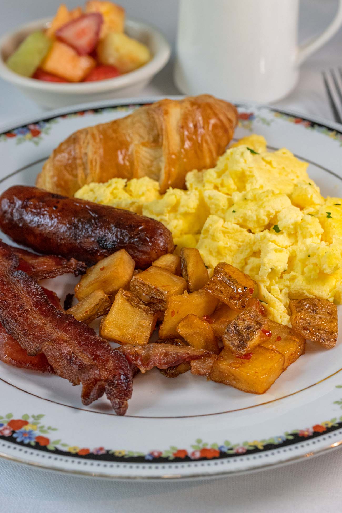 Complimentary breakfast buffet plate with fluffy scrambled eggs, crispy bacon strips, breakfast sausage links, golden roasted breakfast potatoes, fresh croissant and fruit salad at boutique Hotel Fauchere Milford PA Poconos