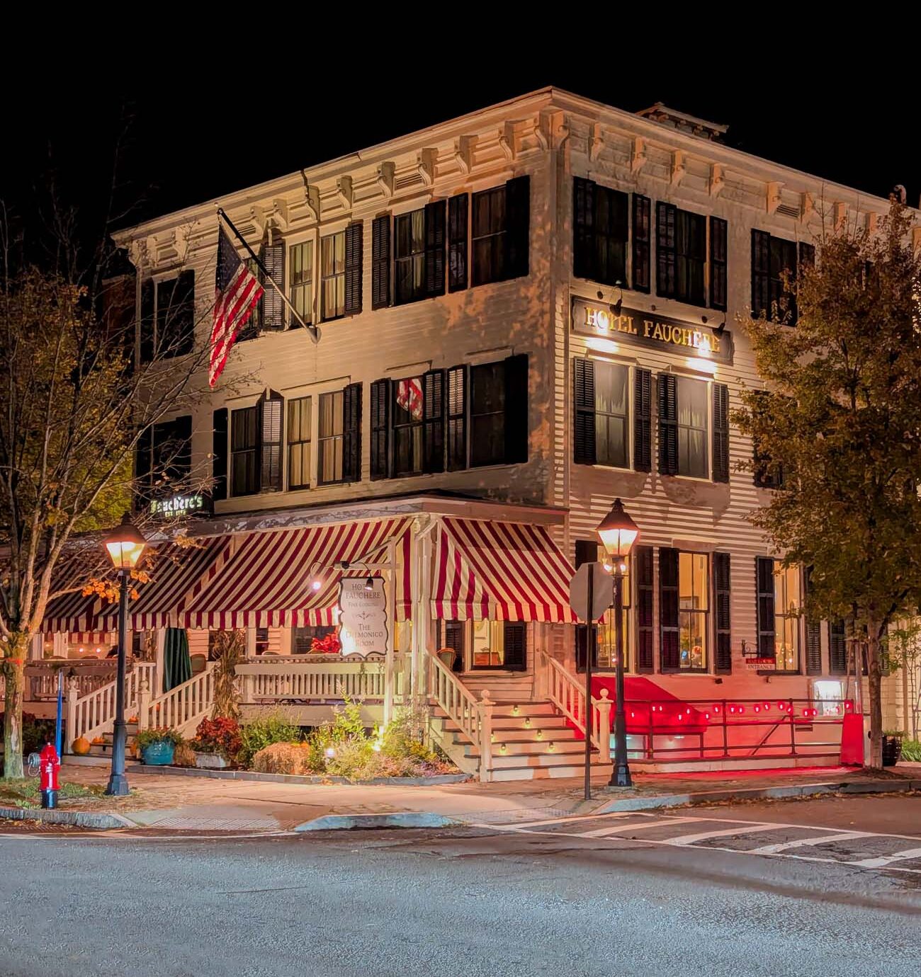 Historic Michelin Key Hotel Fauchere Victorian building illuminated at night with red and white striped awning, American flag, ornate white porch railings and vintage street lamps on Broad Street in downtown Milford Pennsylvania fall evening